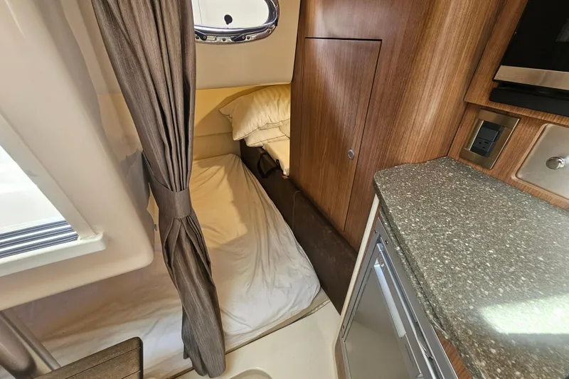 Slide: The Image of 2018 Boston Whaler 315 Conquest cabin interior with bed, curtain, and kitchenette. - 32