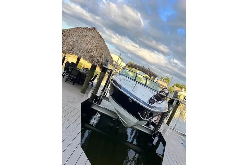 The Image of 2009 Formula 350 Sun Sport boat docked near a thatched-roof hut under a cloudy sky. - 0