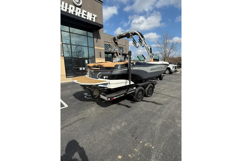 Slide: The Image of 2019 MasterCraft XT20 boat on trailer outside dealership, under clear blue sky. - 2