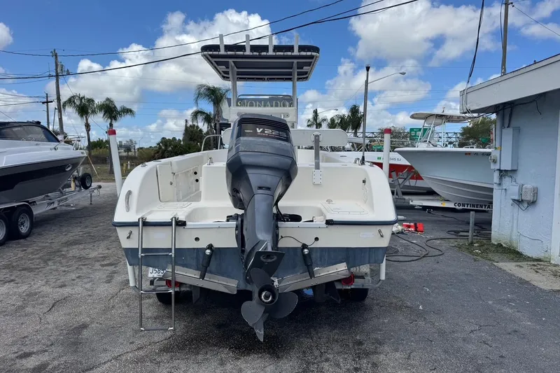 Slide: The Image of 1998 Legacy Boat 220 Sea Era with outboard motor, parked outdoors under blue sky. - 4