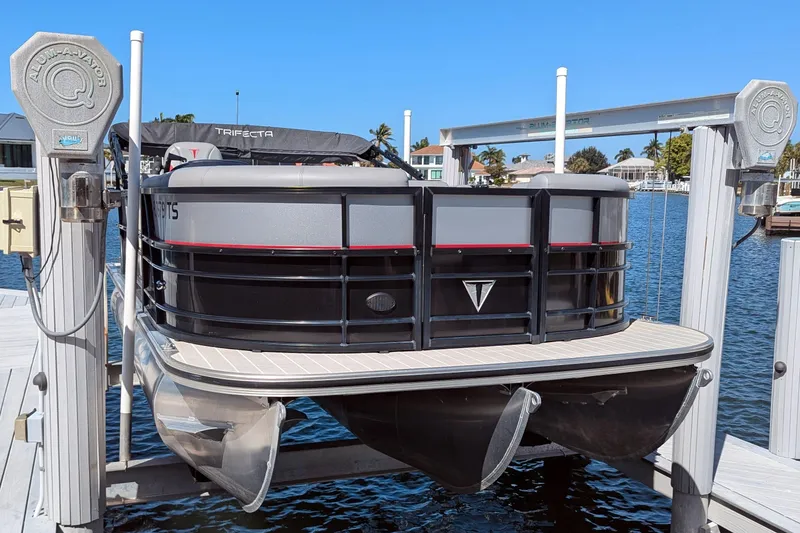 Slide: The Image of 2023 Trifecta 20CC 2.75 pontoon boat docked on a lift by the water. - 14