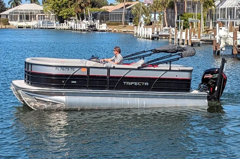 Slide: The Image of 2023 Trifecta 20CC 2.75 pontoon boat cruising on a sunny waterfront. - 2