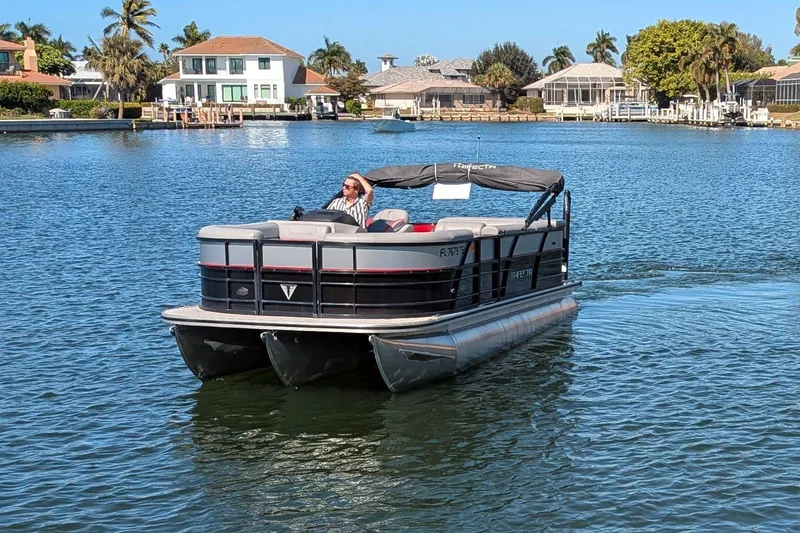 Slide: The Image of 2023 Trifecta 20CC 2.75 pontoon boat cruising on a sunny waterfront. - 3