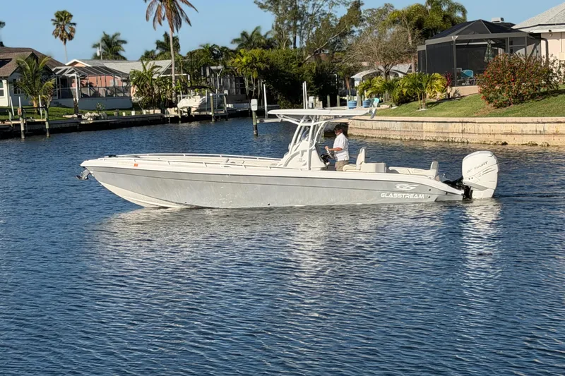 Slide: The Image of 2022 Glasstream 328 Pro-XS boat cruising on a sunny waterfront with palm trees. - 2
