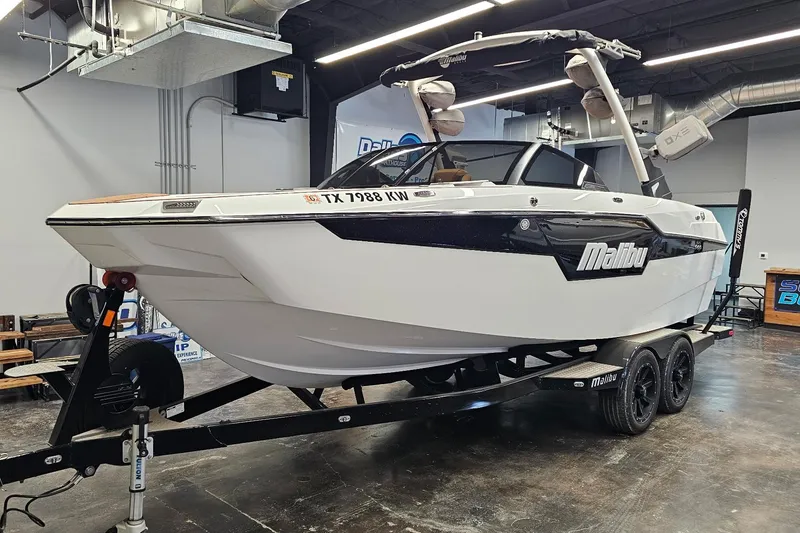 The Image of 2023 Malibu M220 boat on trailer in showroom, featuring sleek design and modern features. - 0