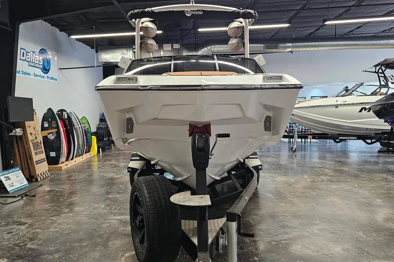 Slide: The Image of 2023 Malibu M220 boat on trailer in showroom, surrounded by surfboards. - 24