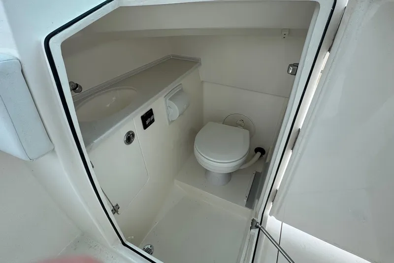 Slide: The Image of 2024 Cobia 240 Dual Console boat interior with compact marine toilet and sink. - 12