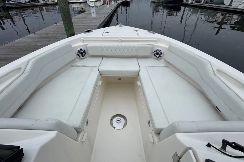Slide: The Image of 2024 Cobia 240 Dual Console boat interior with white seating and speakers at a marina. - 14
