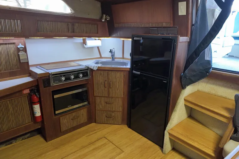 Slide: The Image of 1986 Sea Ray 390 Express Cruiser kitchen with stove, microwave, fridge, and wooden cabinetry. - 39
