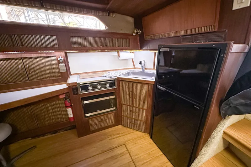 Slide: The Image of 1986 Sea Ray 390 Express Cruiser kitchen with wood cabinetry, stove, sink, and refrigerator. - 64