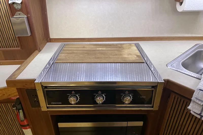 Slide: The Image of 1986 Sea Ray 390 Express Cruiser kitchen with stove, sink, and wooden accents. - 67