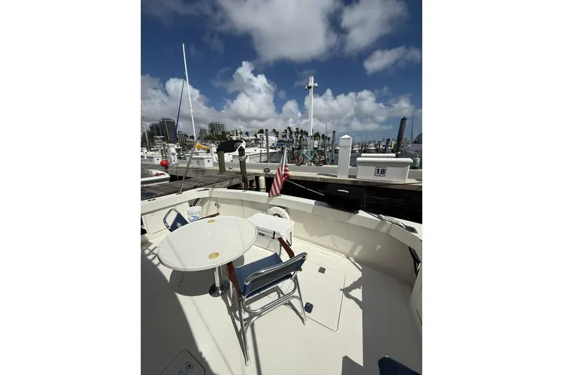 Slide: The Image of 1988 Bertram 43 Flybridge yacht docked, featuring outdoor seating and marina view. - 20