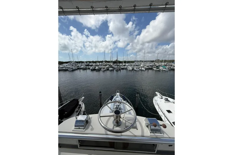 Slide: The Image of 1988 Bertram 43 Flybridge yacht overlooking marina with sailboats under a cloudy sky. - 79