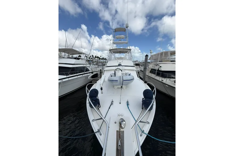 Slide: The Image of 1988 Bertram 43 Flybridge yacht docked, showcasing sleek design and spacious deck under a cloudy sky. - 89