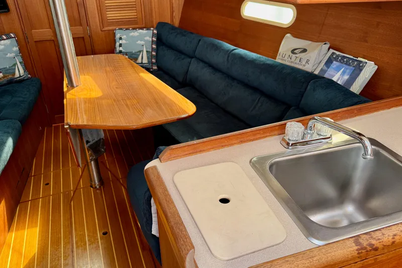 Slide: The Image of Interior of 2001 Hunter 320 sailboat with wooden table, blue seating, and kitchenette sink. - 24