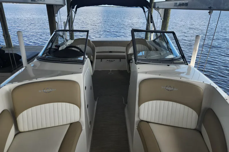 Slide: The Image of 2018 Stingray 235 LR boat interior with tan and white seating, docked by the water. - 12