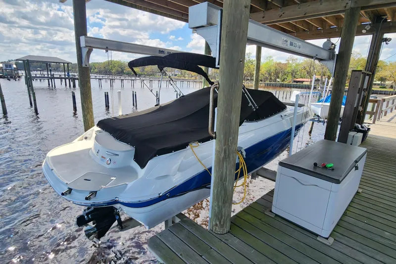 Slide: The Image of 2018 Stingray 235 LR boat docked under a wooden canopy on a sunny day. - 2