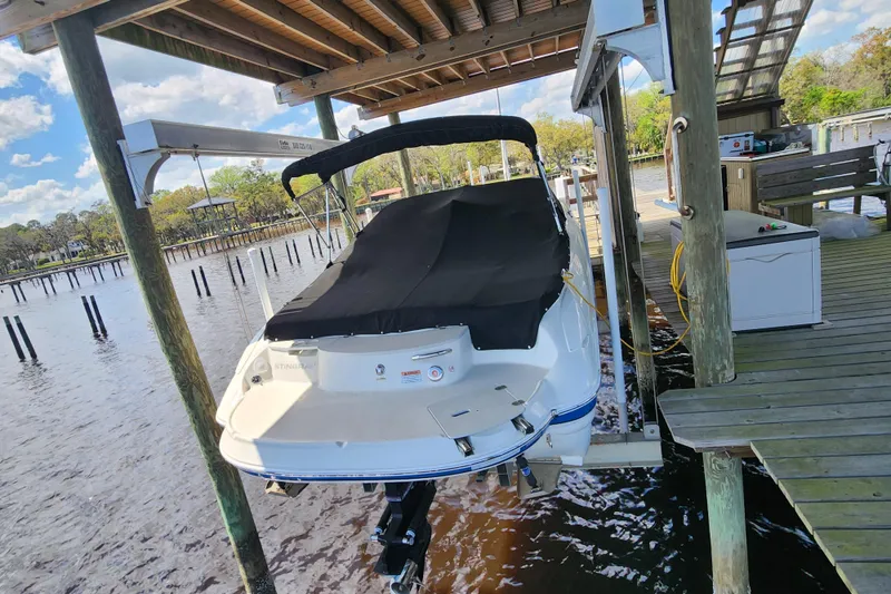 Slide: The Image of 2018 Stingray 235 LR boat docked under a wooden canopy on a sunny day. - 3