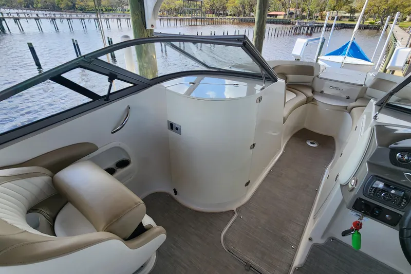 Slide: The Image of 2018 Stingray 235 LR boat interior with seating and dashboard, docked by a scenic waterfront. - 33
