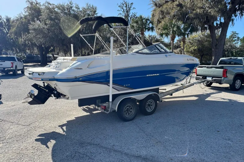 Slide: The Image of 2018 Stingray 235 LR boat on trailer, parked outdoors with trees in background. - 5