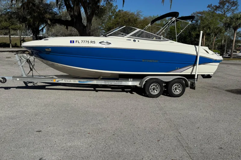 Slide: The Image of 2018 Stingray 235 LR boat on trailer, blue and white design, parked outdoors. - 6