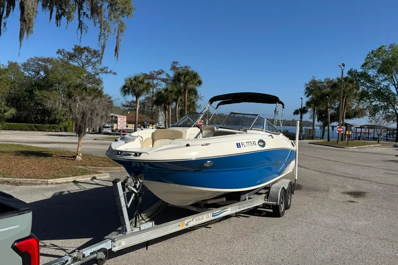 Slide: The Image of 2018 Stingray 235 LR boat on trailer in sunny parking lot near palm trees. - 7