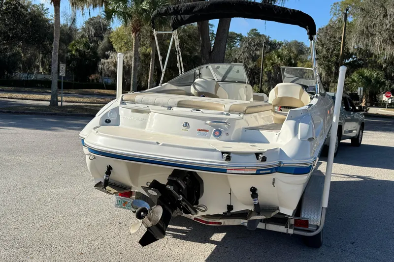 Slide: The Image of 2018 Stingray 235 LR boat on trailer, parked outdoors with trees in background. - 8
