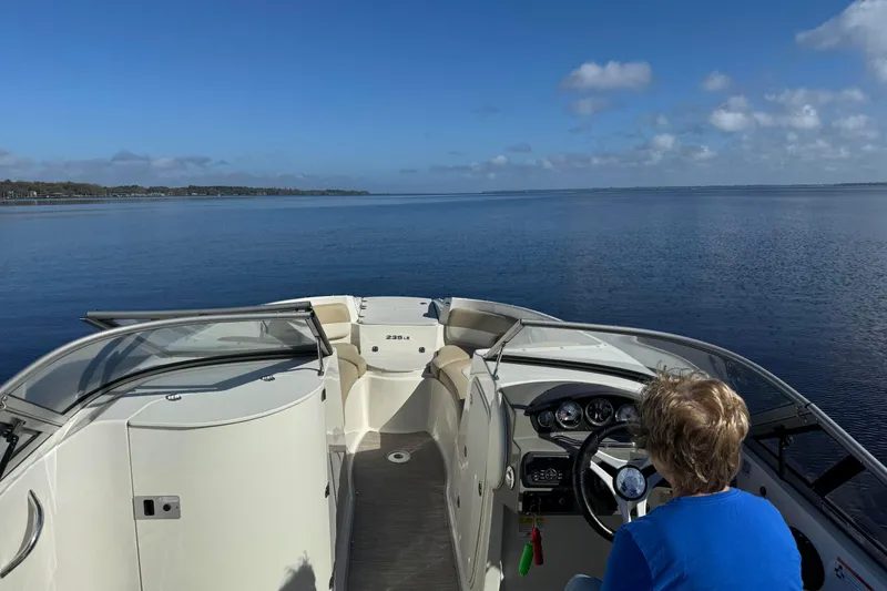 Slide: The Image of 2018 Stingray 235 LR boat cruising on a calm lake under a clear blue sky. - 83
