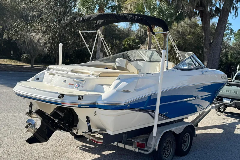 Slide: The Image of 2018 Stingray 235 LR boat on trailer, parked outdoors with trees in background. - 9