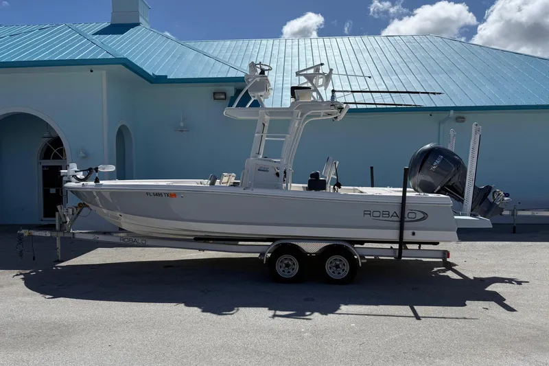 The Image of 2023 Robalo 246 Cayman SD boat on trailer, parked near a blue building. - 0