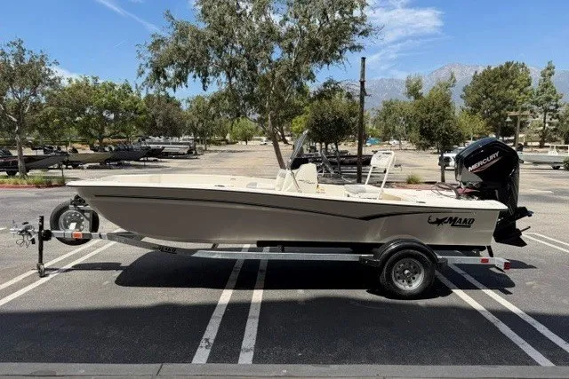 Slide: The Image of 2026 Mako Pro Skiff 17 CC boat on trailer in parking lot, surrounded by trees. - 1