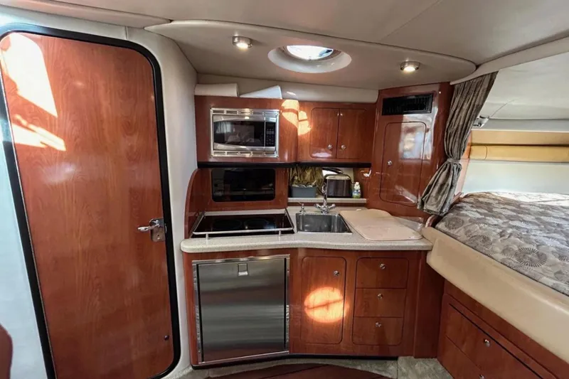 Slide: The Image of 2015 Crownline 350 SY yacht interior with kitchenette, wood cabinetry, and cozy sleeping area. - 10