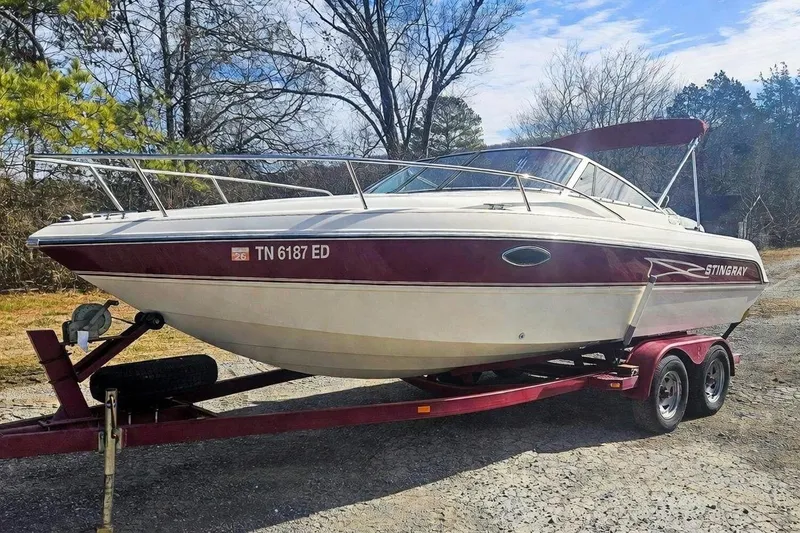 The Image of 1999 Stingray 220 CS boat on trailer, parked outdoors, with maroon and white design. - 0