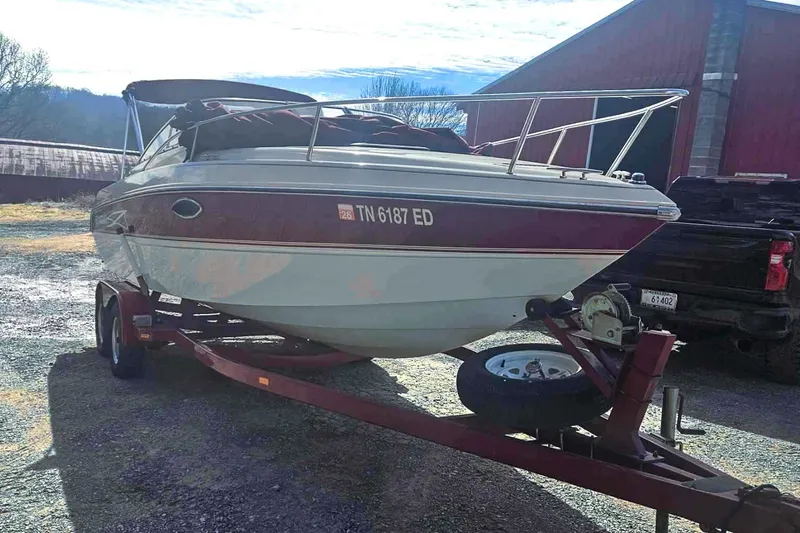 Slide: The Image of 1999 Stingray 220 CS boat on trailer, parked outdoors near a barn. - 1