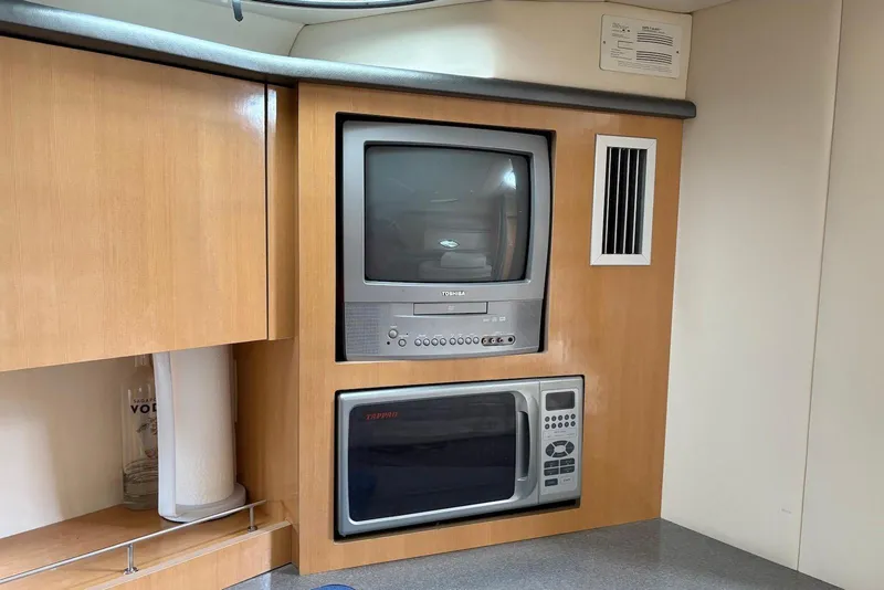 Slide: The Image of 2004 Maxum 3100 SE interior with built-in TV and microwave in wooden cabinetry. - 13