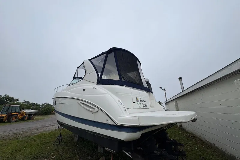 Slide: The Image of 2004 Maxum 3100 SE boat with canopy, parked on land near a building. - 2