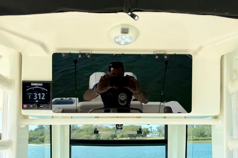 Slide: The Image of 2024 Boston Whaler 250 Outrage dashboard with Simrad display and rearview mirror reflection. - 31