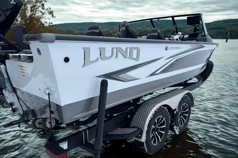 Slide: The Image of 2023 Lund 2175 Pro-V boat on trailer by the water, showcasing sleek design. - 2