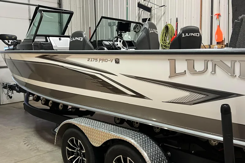 Slide: The Image of 2023 Lund 2175 Pro-V boat in a garage, featuring sleek design and modern seating. - 68