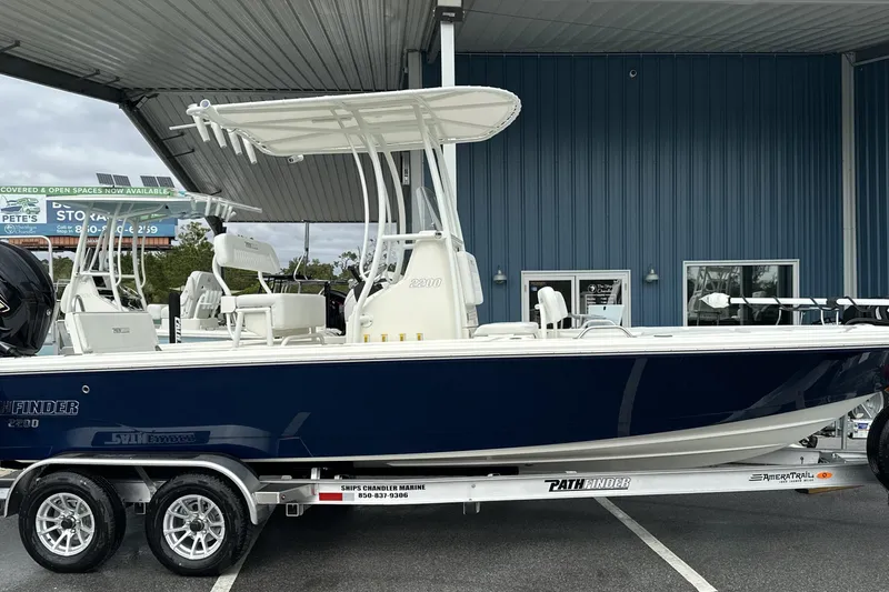 Slide: The Image of 2026 Pathfinder 2200 TRS boat on trailer, blue hull, under metal canopy. - 17