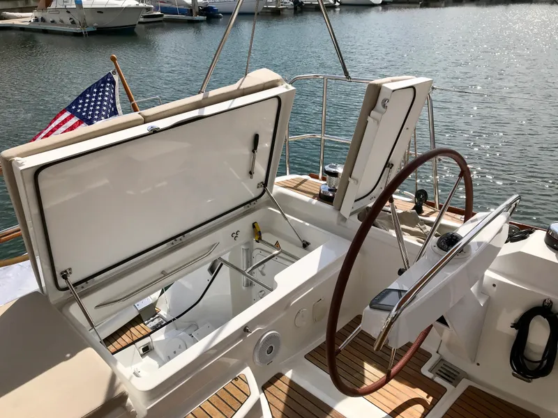 Slide: The Image of 2014 Jeanneau 57 yacht cockpit with open storage, steering wheel, and American flag. - 23