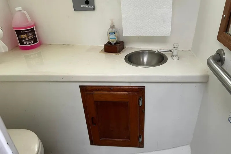 Slide: The Image of Compact bathroom with sink, wooden cabinet, and cleaning supplies on a Young Brothers 1985 model 40 boat. - 15