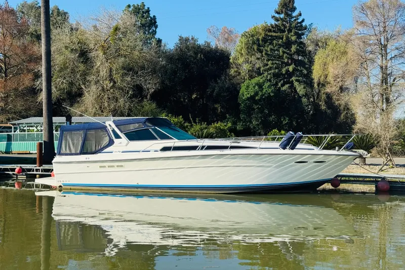 The Image of 1989 Sea Ray 390 Express Cruiser docked on calm water, surrounded by trees. - 0