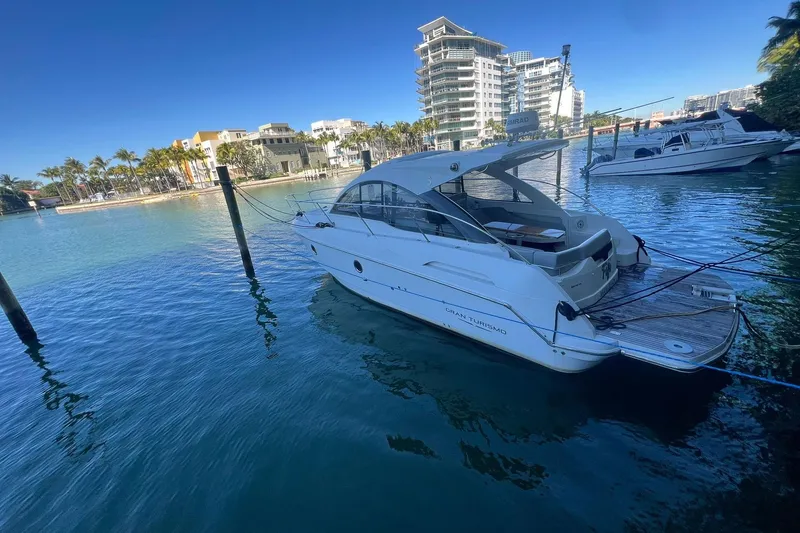 Slide: The Image of 2013 Beneteau Flyer GT 34 yacht docked in a scenic marina with modern buildings. - 2