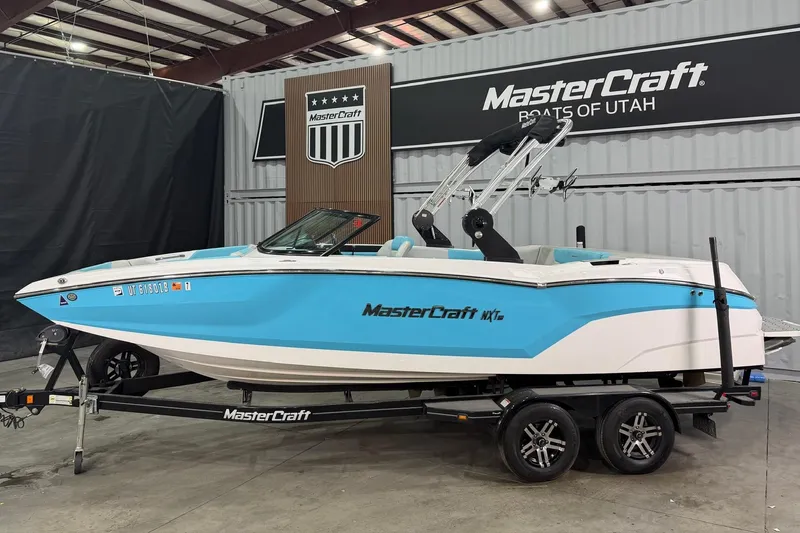 The Image of 2020 MasterCraft NXT22 boat in showroom, blue and white design, on trailer. - 1