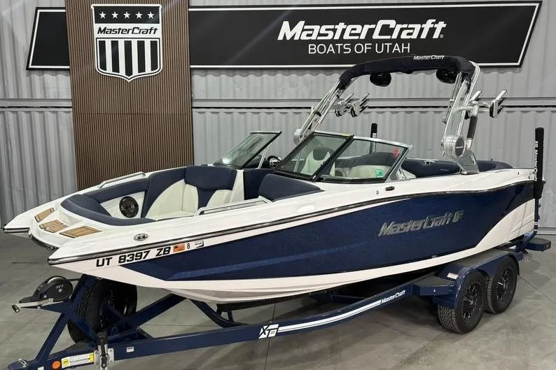 The Image of 2019 MasterCraft XT22 boat in showroom, blue and white design, on trailer. - 1