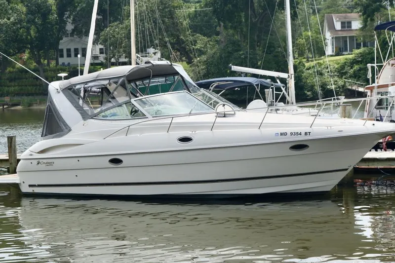 The Image of 2004 Cruisers Yachts 320 Express docked on a calm lake with lush greenery. - 0