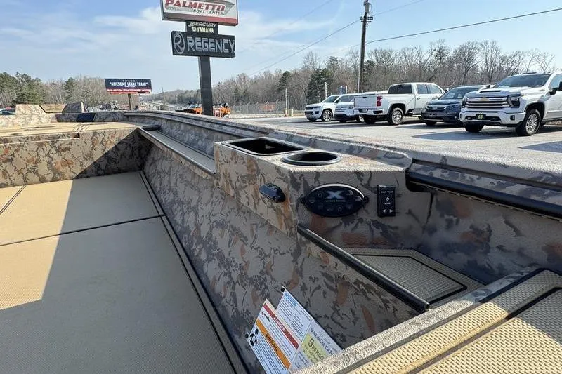 Slide: The Image of 2026 Xpress X18DB boat interior with camouflage design, parked outdoors near dealership. - 8