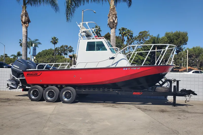 The Image of 1989 Boston Whaler Challenger boat on trailer, red hull, parked outdoors with palm trees. - 0