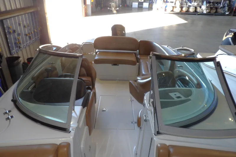 Slide: The Image of 2023 Crownline 250 XSS boat interior with brown seating and dual windshields in a showroom. - 16